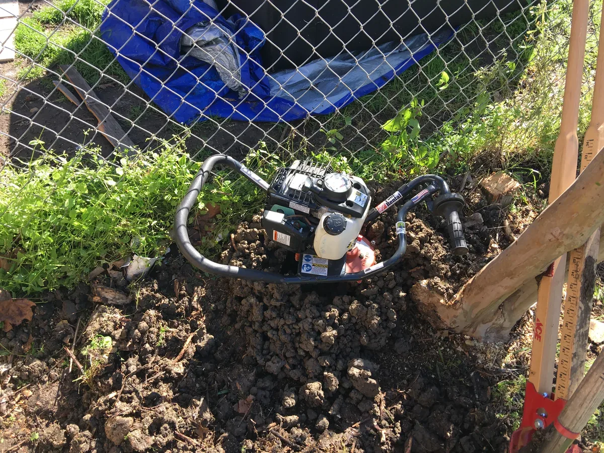 Excavated soil and equipment along a chain link fence during root and stump removal
