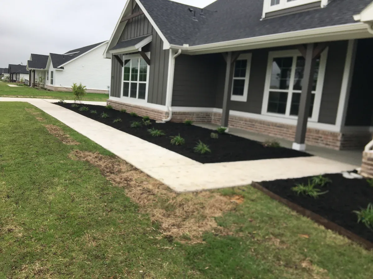 Mulch bed and shrubs along a home foundation next to a concrete walkway