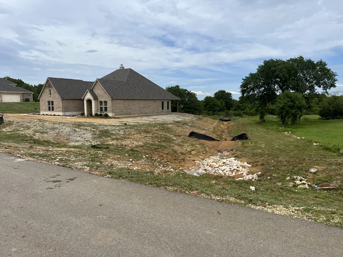 Cleared and graded rural property with exposed soil and a remaining shade tree