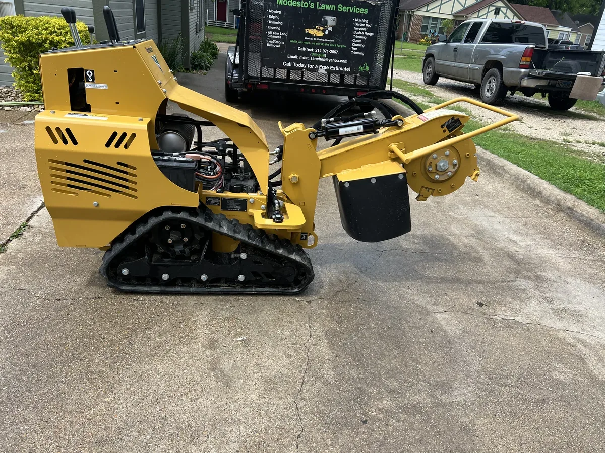 Tracked stump grinder parked on a driveway beside a trailer