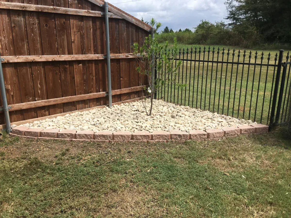 Finished white wash rock bed with stone edging in a fenced backyard corner
